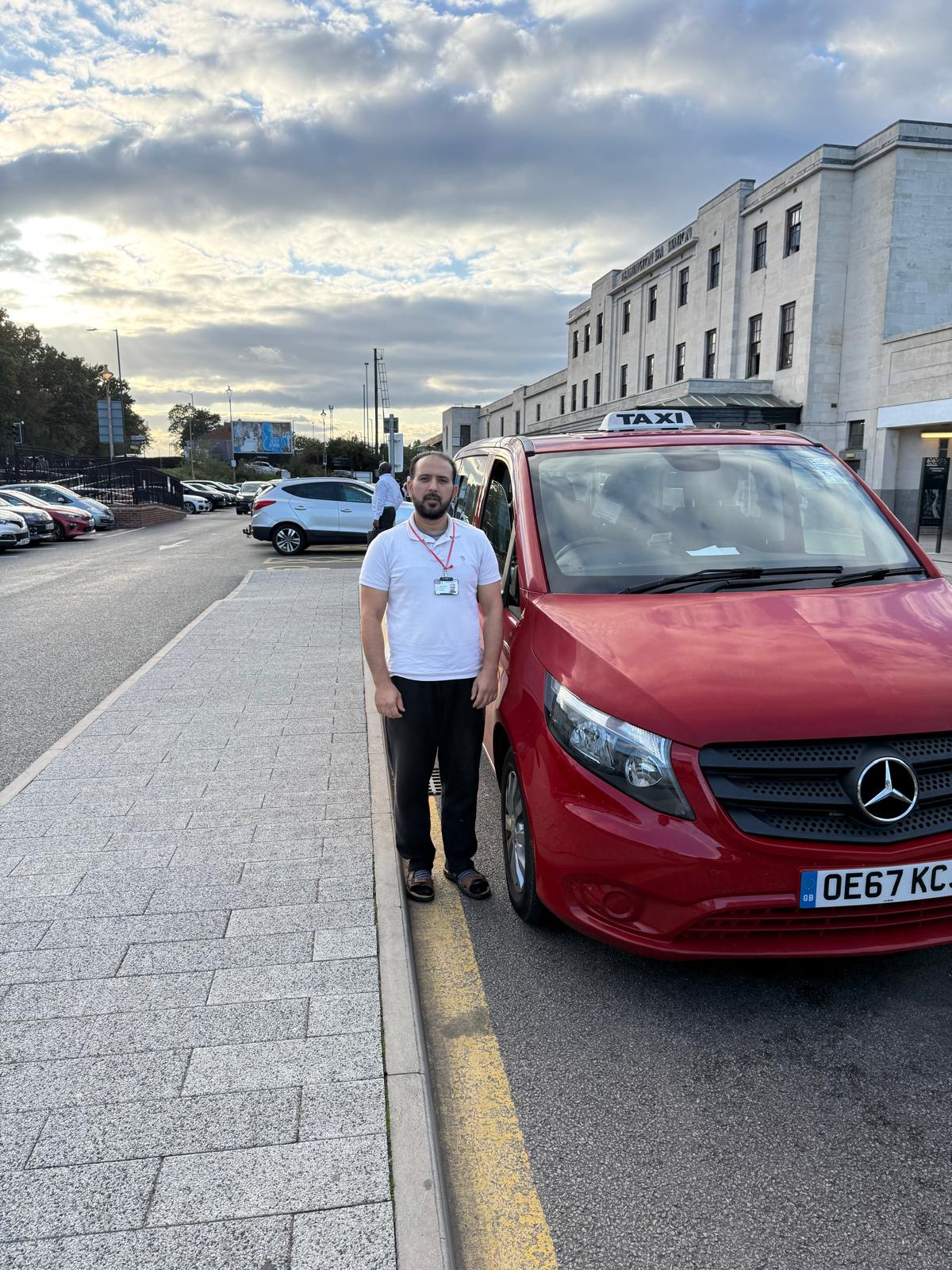 Local Taxi driver beside a red Mercedes taxi in Warwick